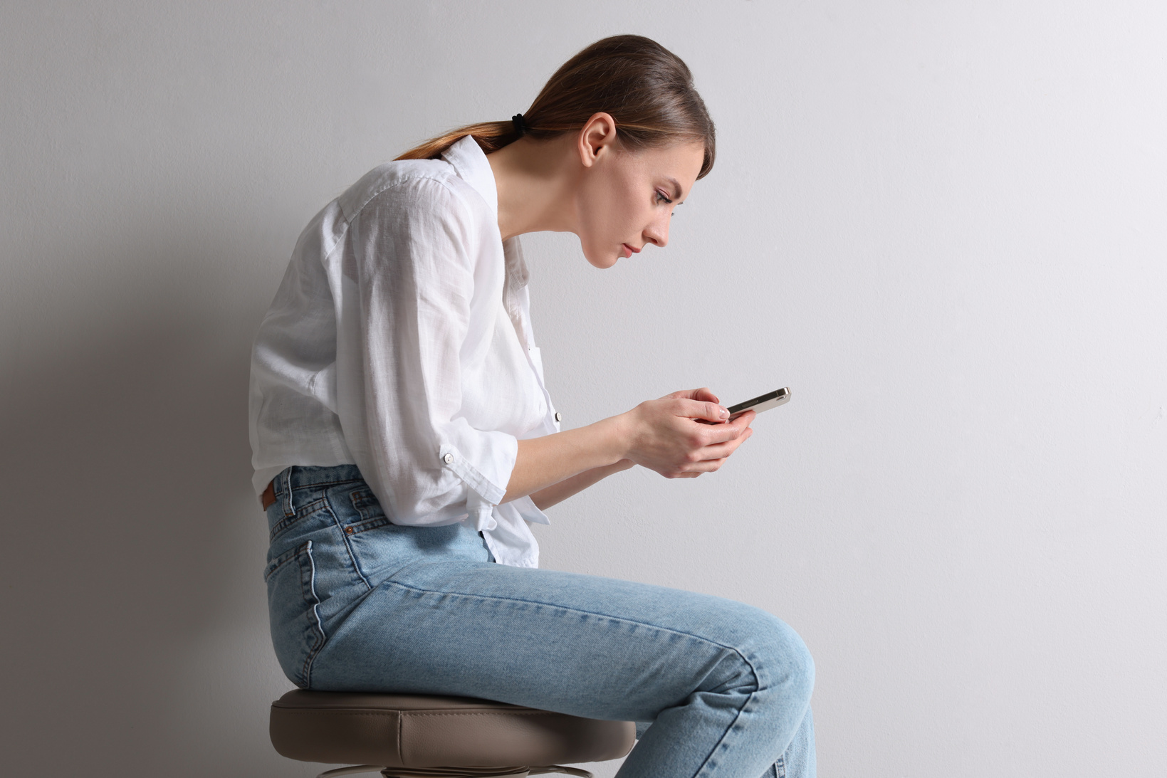 Woman with Bad Posture Using Smartphone While Sitting on Stool a