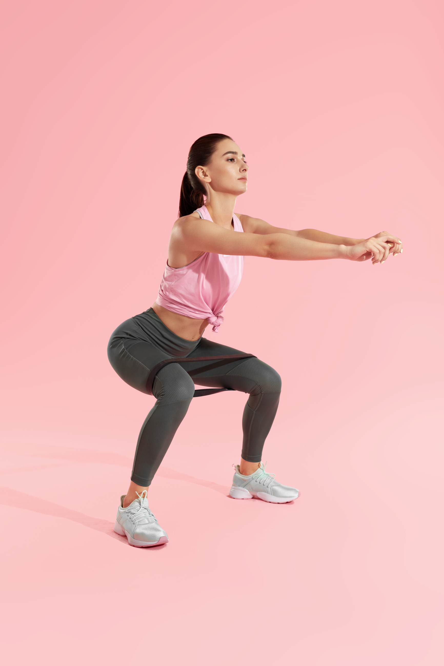 Squats. Woman in sports wear squatting with resistance band